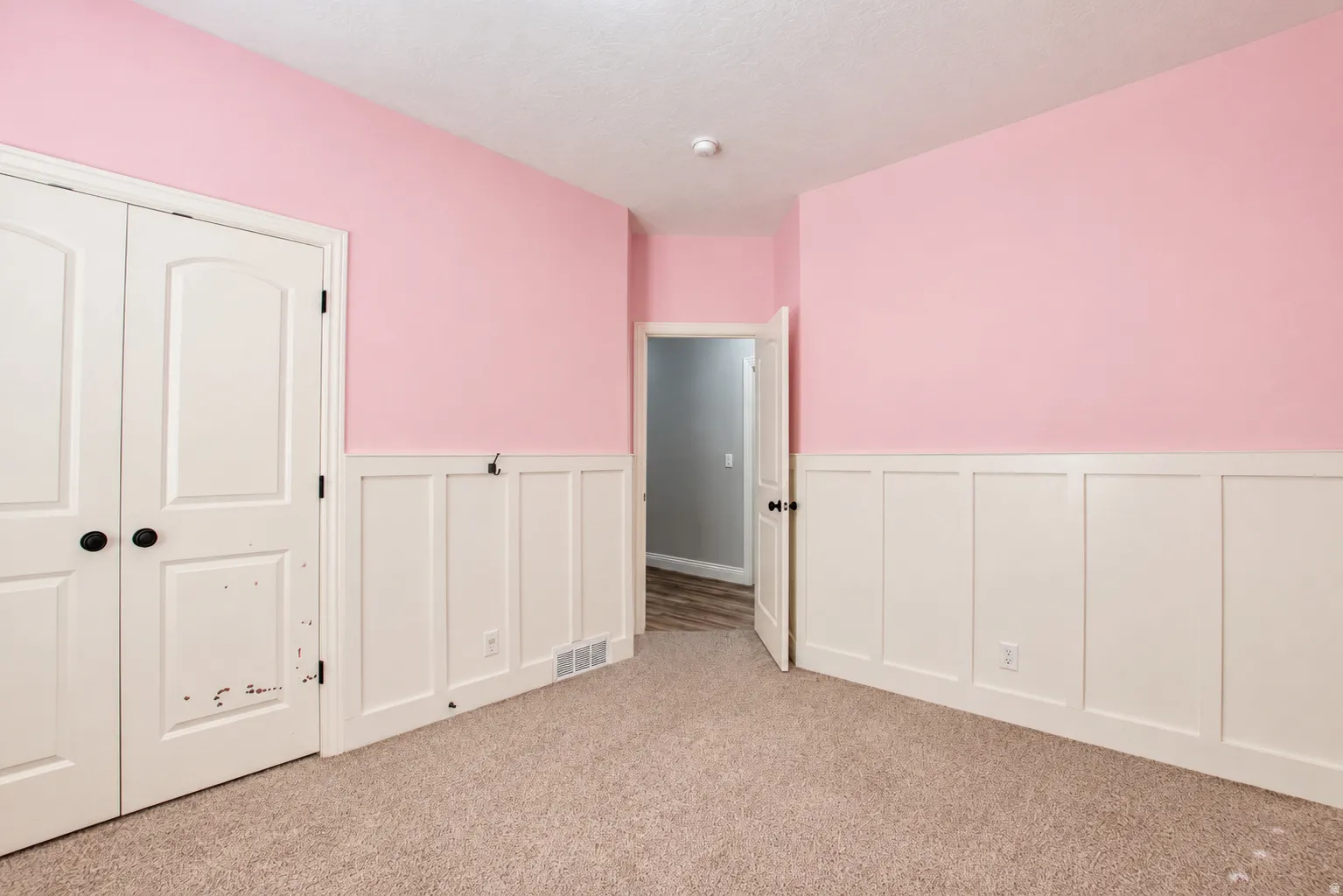 Carpeted room featuring a white board and batten wall treatment, light pink upper walls, and a white ceiling
