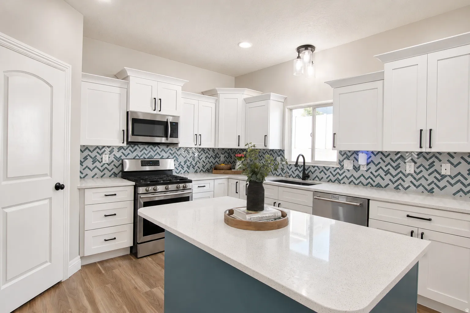 Kitchen featuring white shaker cabinetry, stainless steel appliances, a chevron-patterned backsplash, a central island with a light-colored countertop, and wood-finish flooring