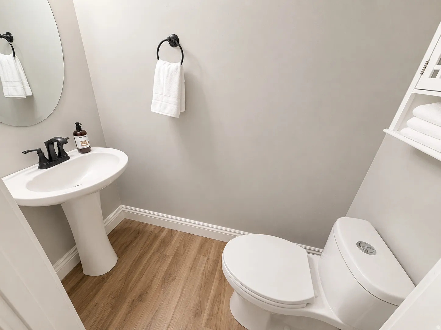 Bathroom featuring a white pedestal sink with a matte black faucet, wood-finish flooring, a contemporary toilet, and a wall-mounted storage unit
