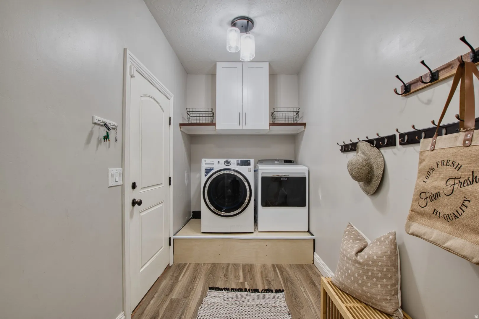 Dedicated laundry area featuring wood-finish flooring and a built-in shelf with upper cabinetry