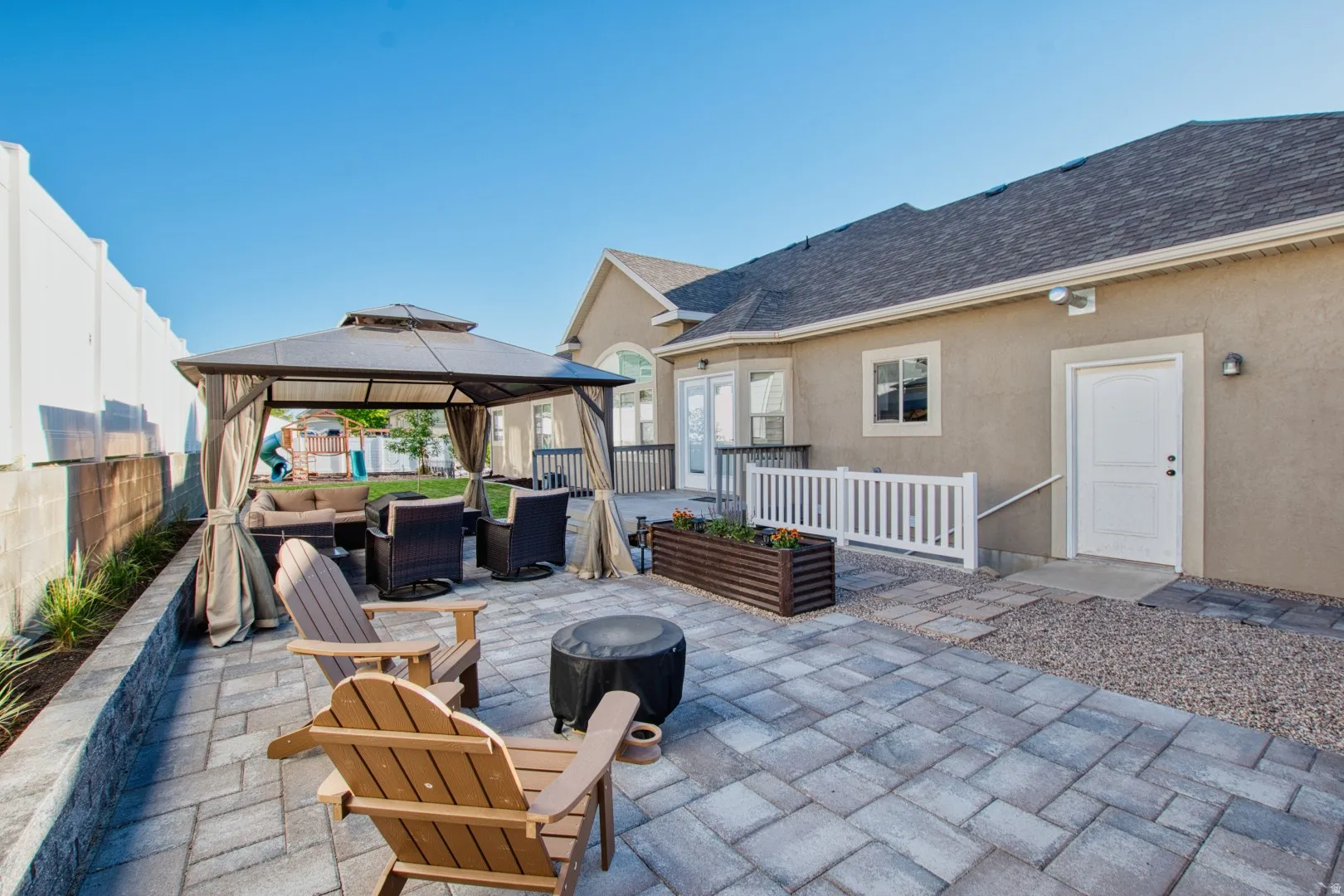 Expansive paver patio featuring a built-in stone retaining wall, gravel accents, and a large gazebo