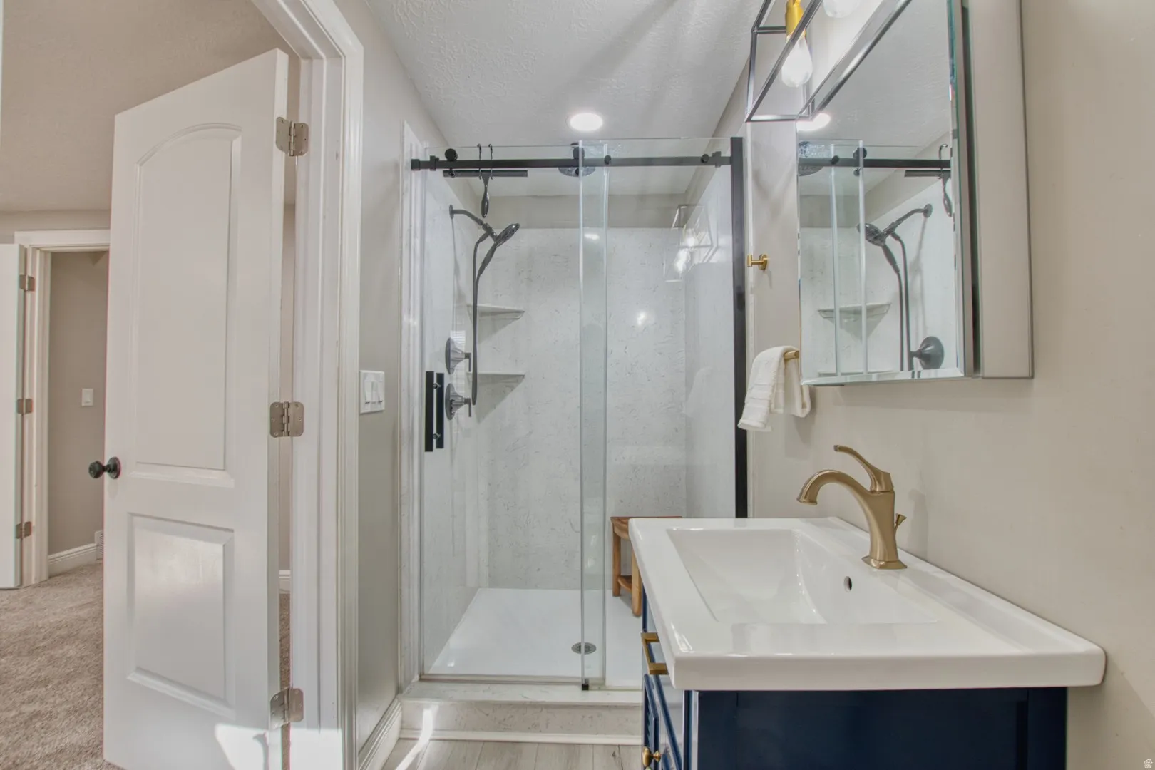 Bathroom featuring a vanity with an integrated sink and gold-tone faucet, a mirrored medicine cabinet, and a glass-enclosed shower with black fixtures.