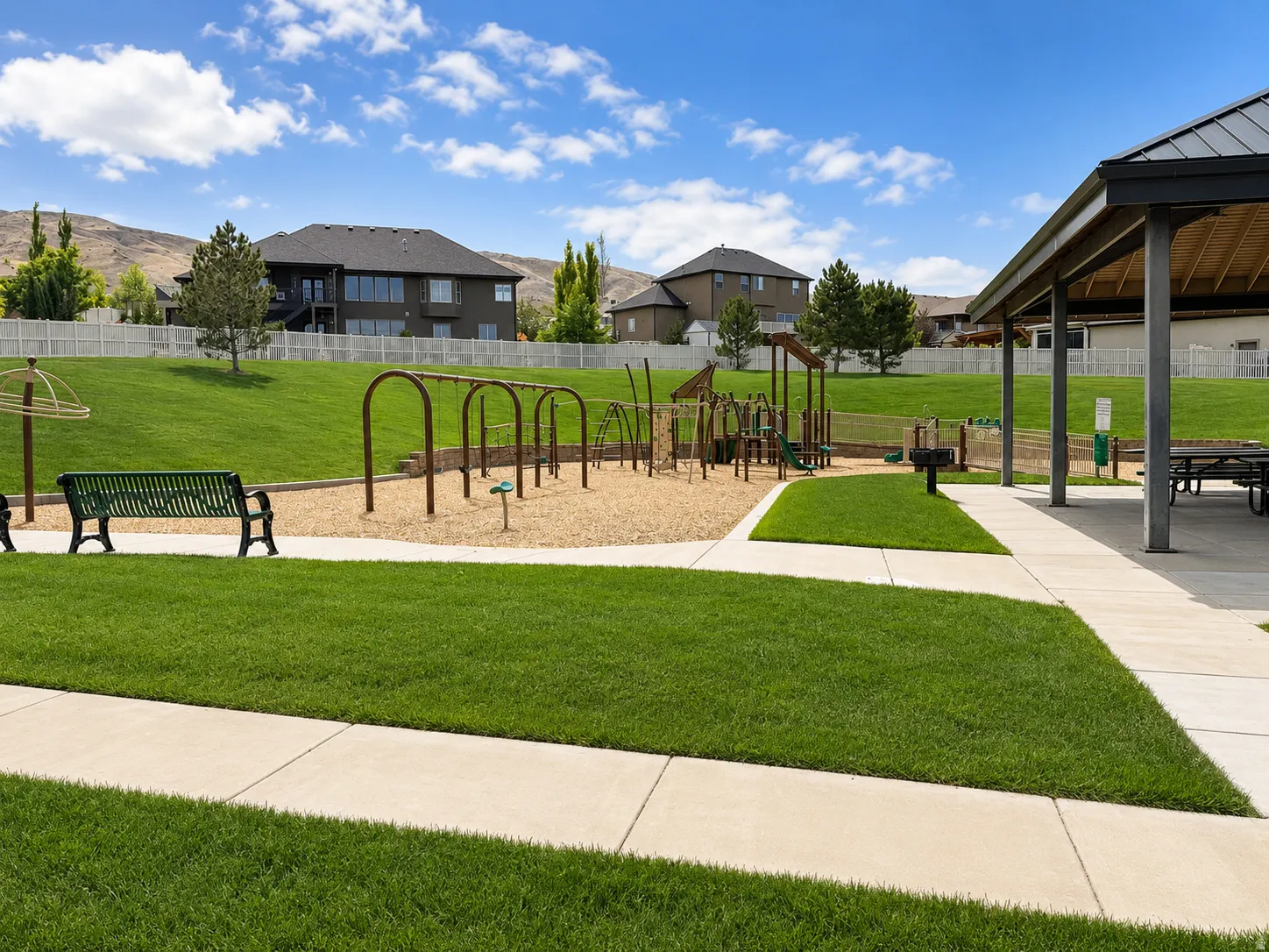 Community park featuring a covered picnic area with tables, a grill station, and a dedicated playground with swings and slides