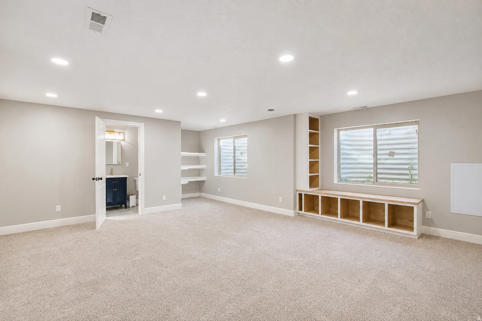Spacious carpeted room featuring recessed lighting, a built-in window bench with storage cubbies, and an integrated tall shelving unit