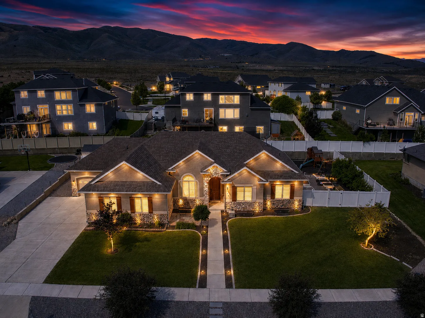 Front exterior featuring stone and stucco finishes, a concrete driveway, and an illuminated walkway