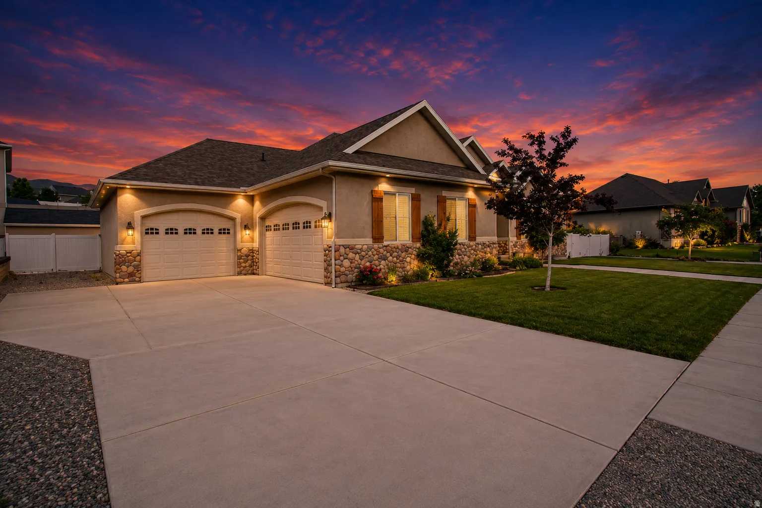 Stucco and stone facade featuring a two-car garage with arched entrances, a concrete driveway, and established landscaping with accent lighting