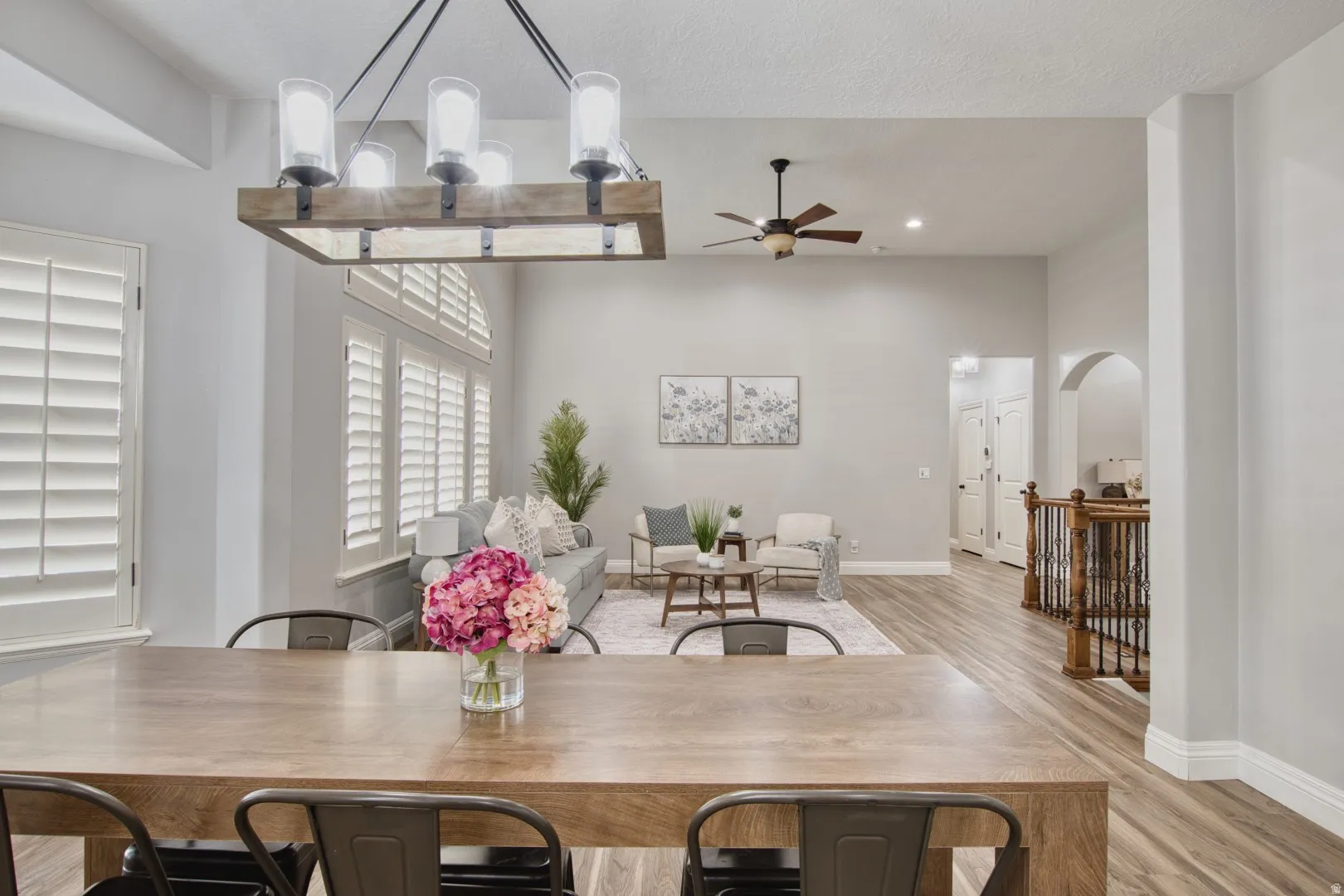 Dining area featuring a wood-finish table with industrial-style chairs, an overhead chandelier with clear glass shades, and plantation shutters
