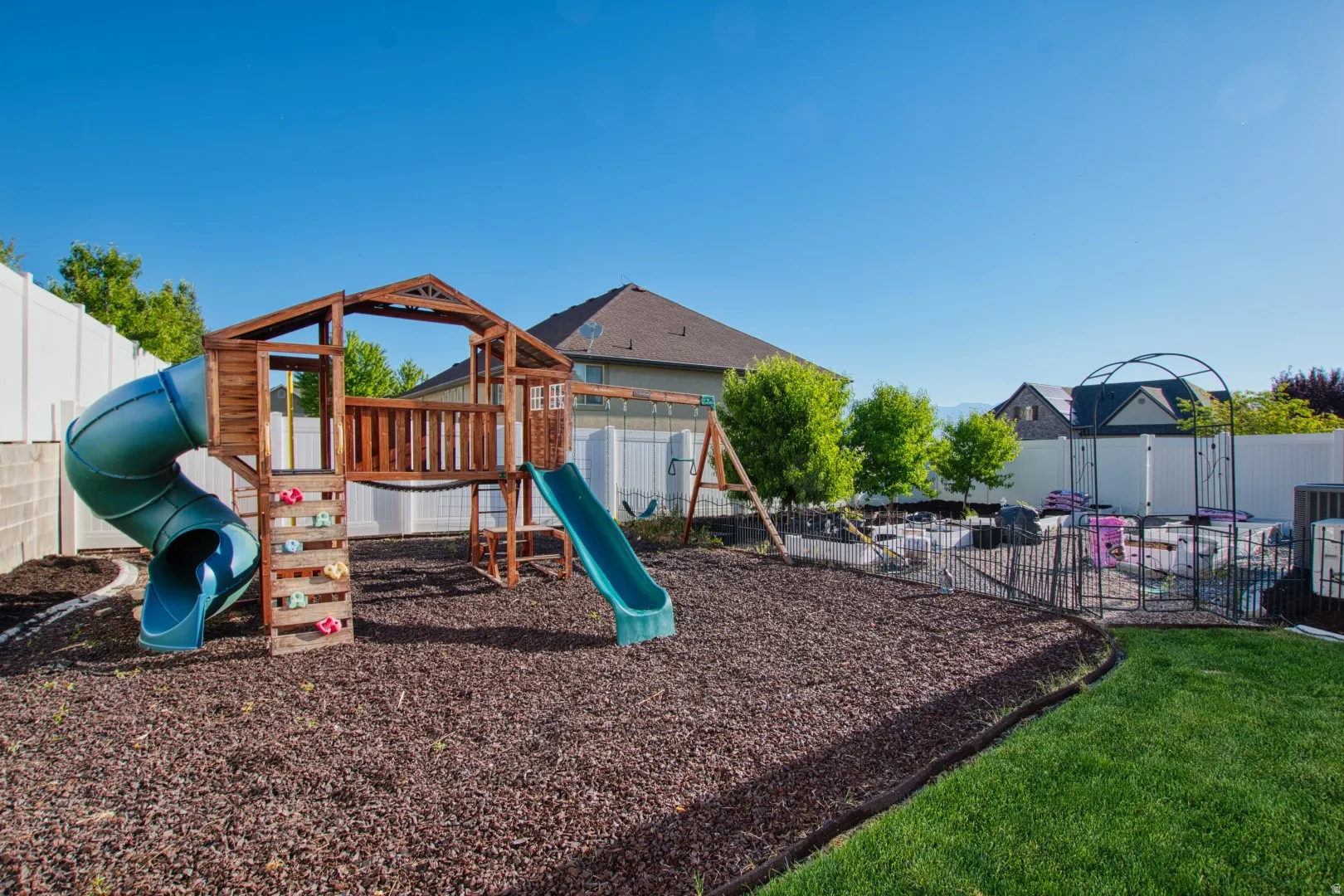 Expansive backyard featuring a wood-structure playset with two slides, a climbing wall, and swing set