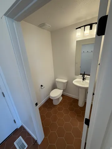 Hexagonal tile flooring, white pedestal sink, black wall-mounted light fixture, white toilet, and white trim