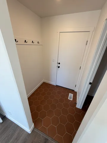 Entryway featuring hexagonal tile flooring, a white paneled door with black hardware, and an integrated coat rack