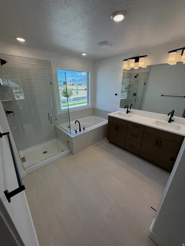 Spacious bathroom featuring a double vanity with stone countertops, a large soaking tub, a glass-enclosed shower with subway tile, light-toned tile flooring, and recessed lighting