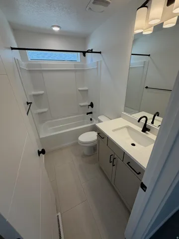 Bathroom featuring a white tub/shower combination, rectangular window, light-toned tile flooring, single vanity with light countertop, and black fixtures