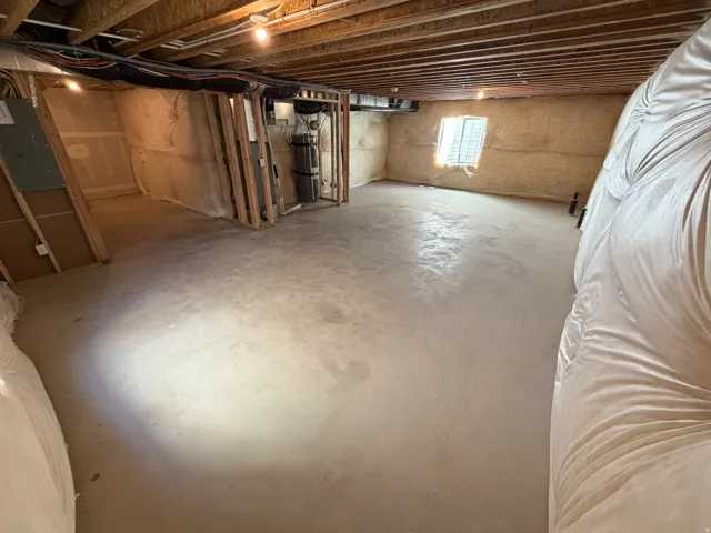 Unfinished lower level featuring exposed wood joists, concrete flooring, and a window providing natural light