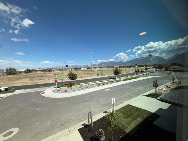 Mountain backdrop, clear sky, asphalt roadway, landscaped median with gravel and plantings, newly laid sod