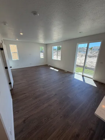 Spacious open-concept room featuring wood-finish flooring, recessed lighting, white walls, multiple windows, and a sliding glass door