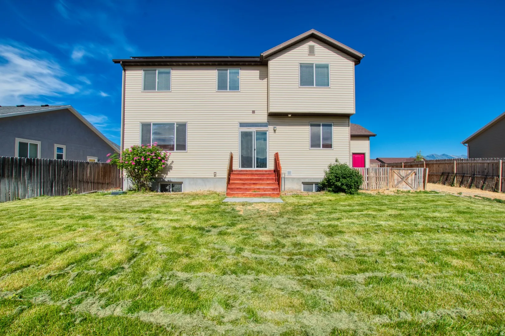 Expansive backyard featuring a green lawn, wood fencing, and a two-story exterior with light-colored siding