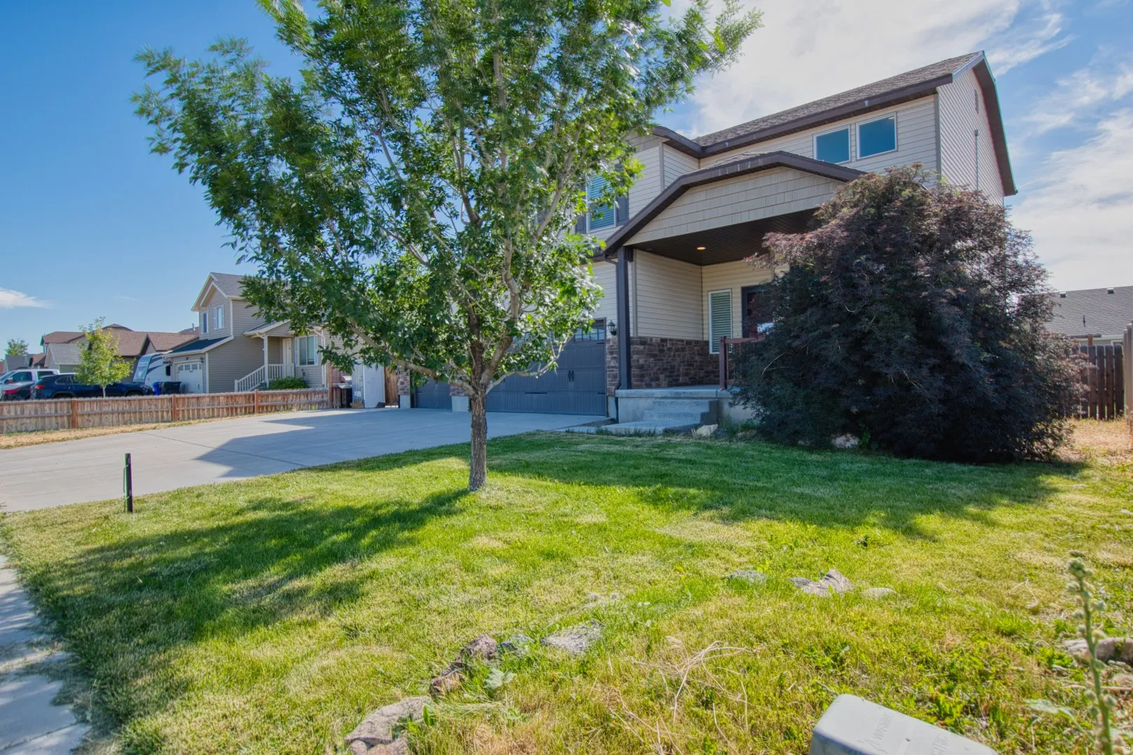 Two-story residence featuring a covered front porch with stone accents, a two-car garage, and a manicured front lawn