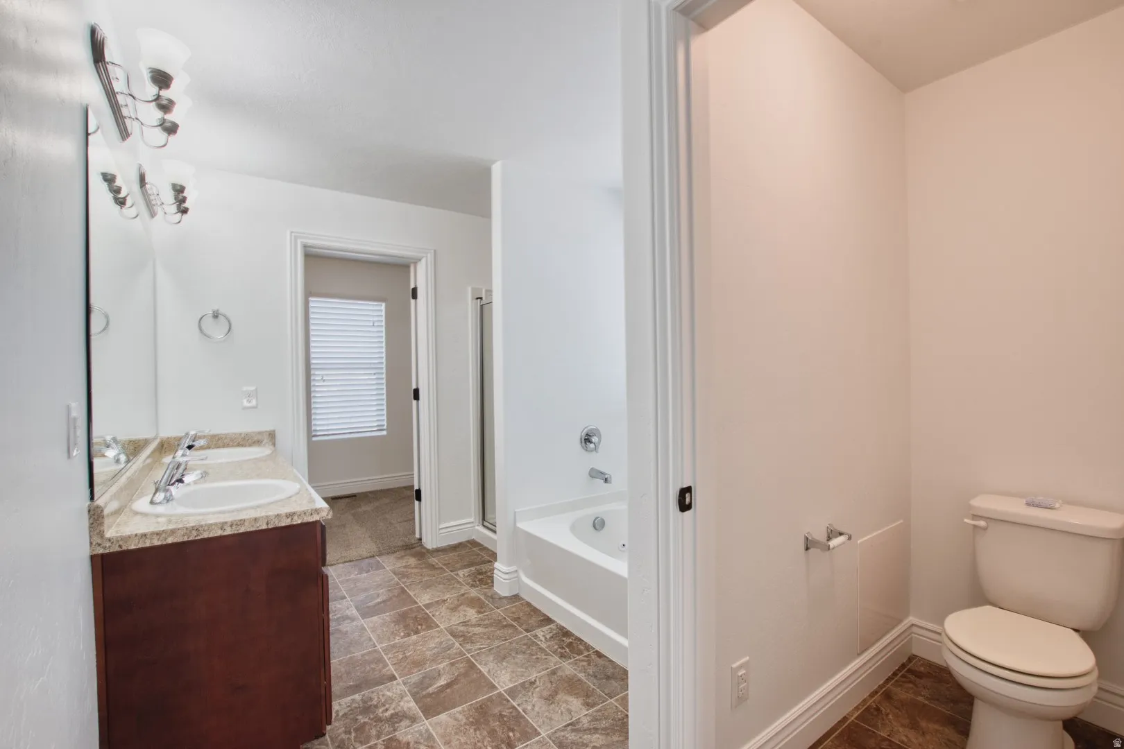 Primary bathroom featuring a spacious dual vanity with a light-toned countertop, a jetted tub, a separate shower enclosure, and a toilet