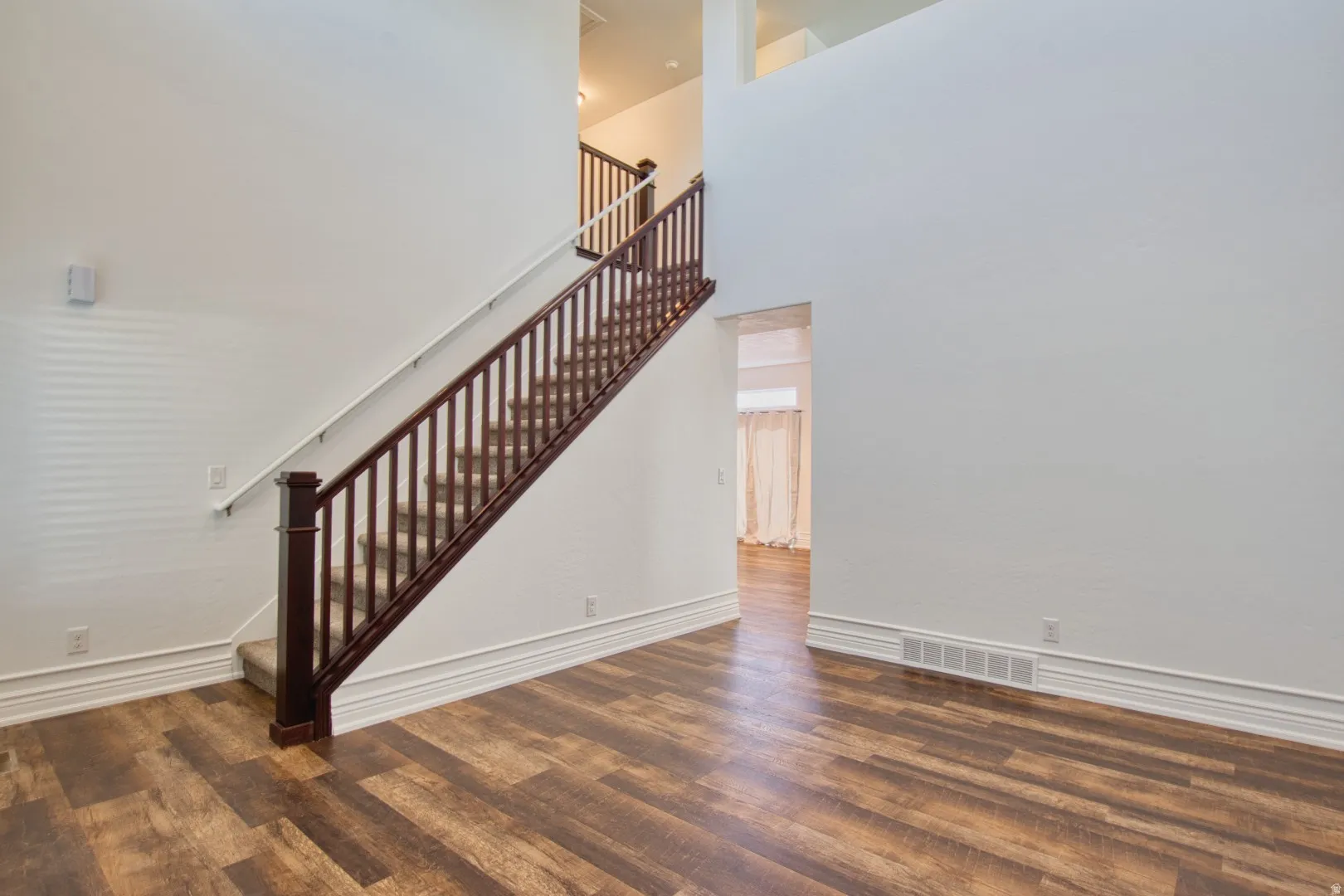 Two-story entry featuring wood-finish flooring, a carpeted staircase with dark wood banister and white spindles, and high ceilings