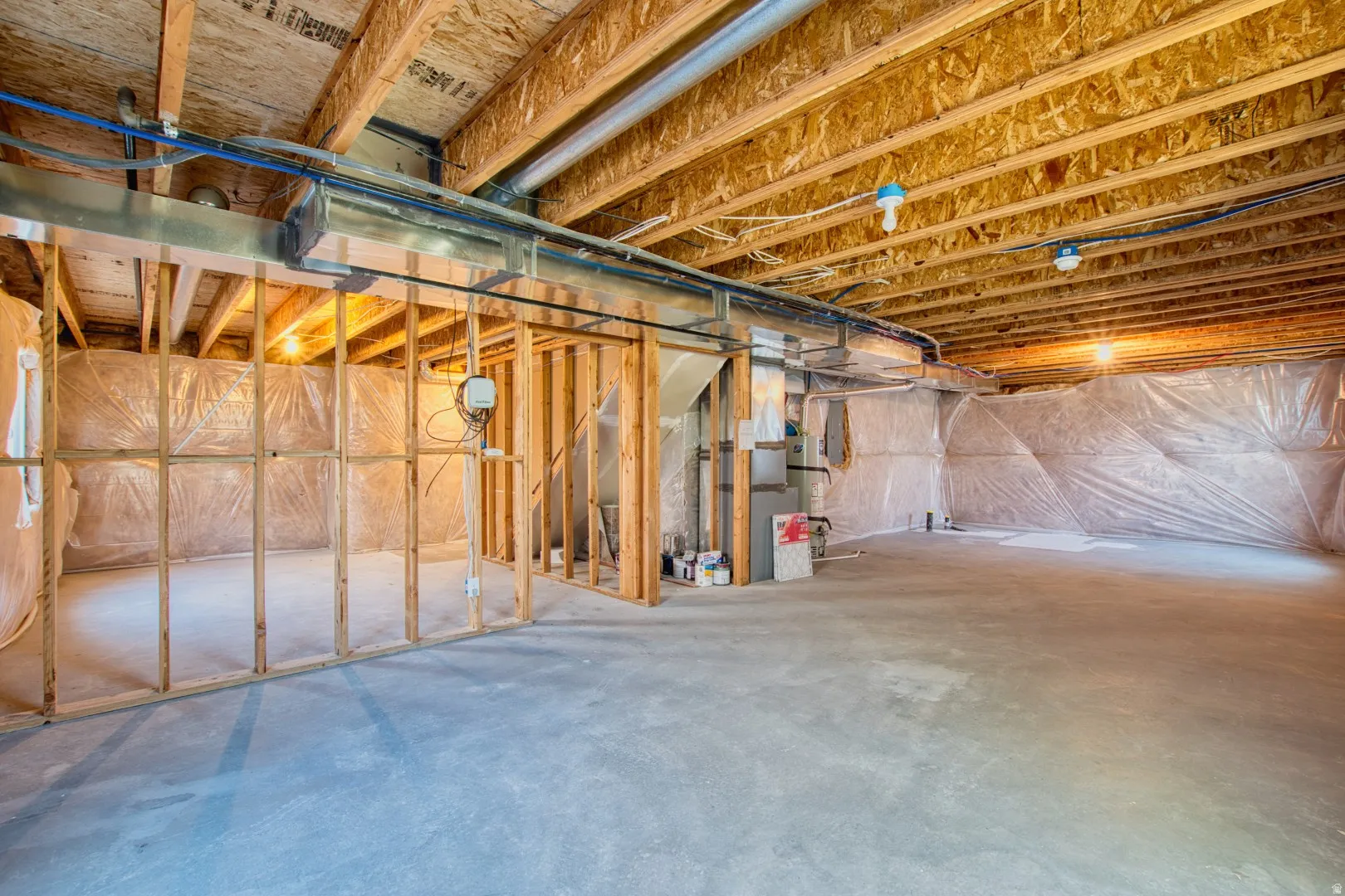 Unfinished basement with exposed ceiling joists, concrete flooring, framed interior walls, visible ductwork, and plumbing lines