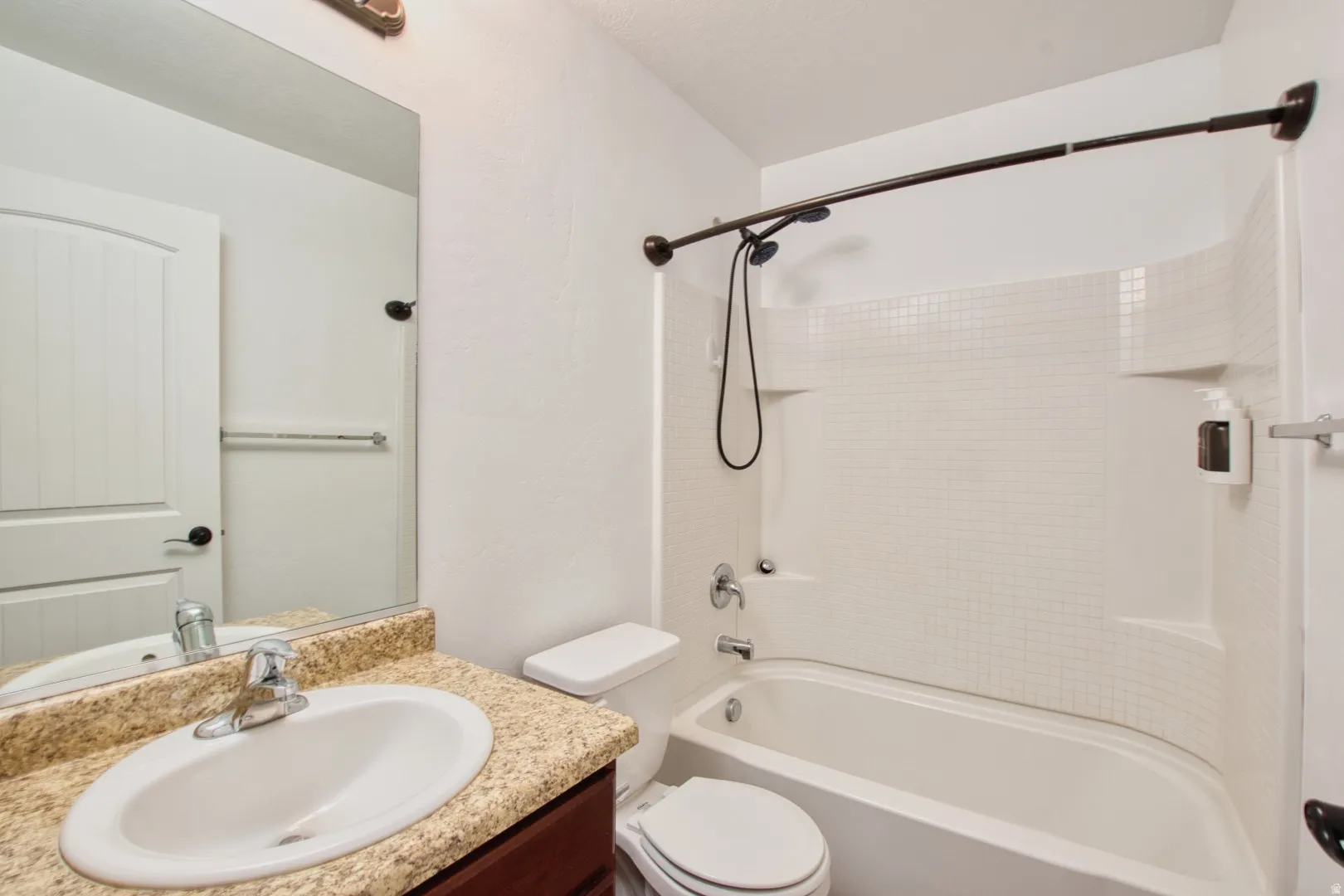 Bathroom featuring a large vanity mirror, a single basin sink with a chrome faucet, a toilet, and a combination shower and tub with a curved shower rod