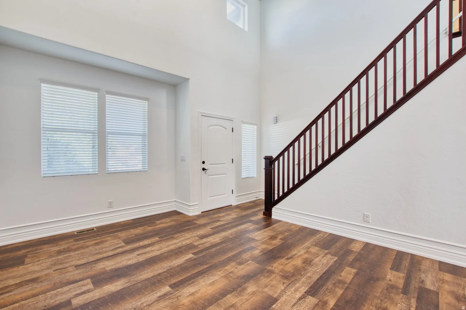Two-story entry foyer featuring wood-finish flooring, a dark wood staircase with spindle railing, and a white paneled entry door