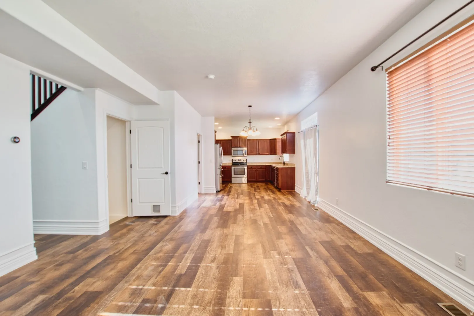 Open-concept living space featuring wood-finish flooring, a contemporary kitchen with wood cabinetry and stainless steel appliances, and abundant natural light from a large window