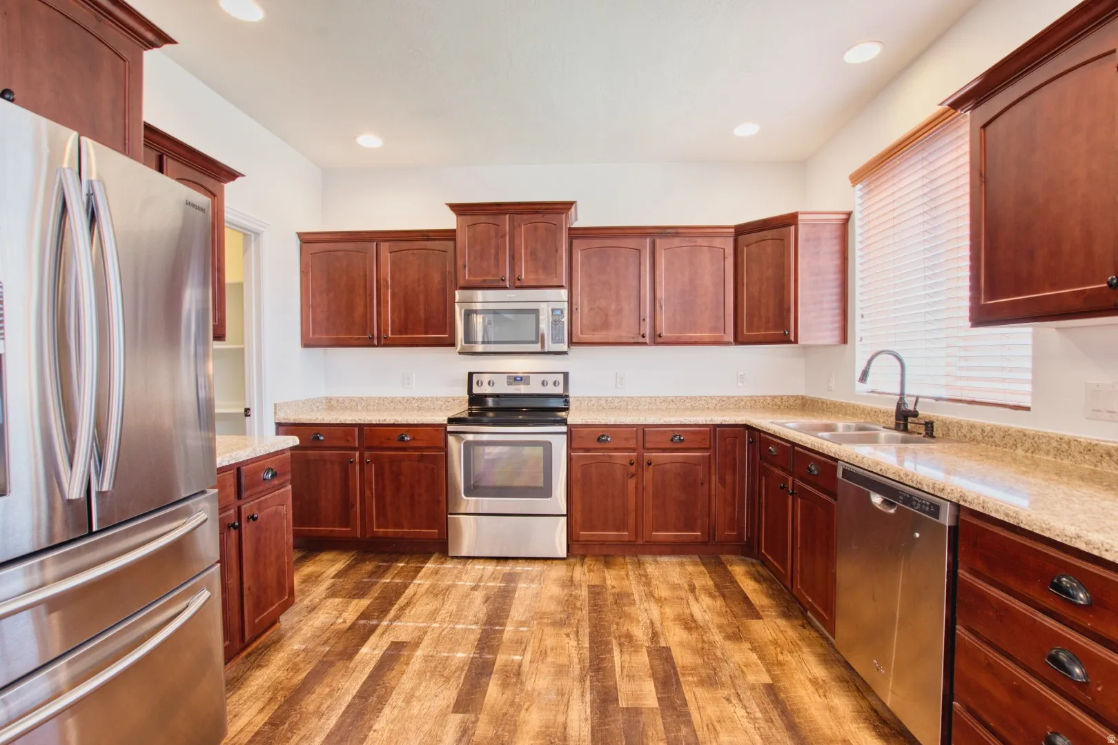 Kitchen featuring wood-finish flooring, dark wood cabinetry, light-toned countertops, and stainless steel appliances including a refrigerator, range, microwave, and dishwasher
