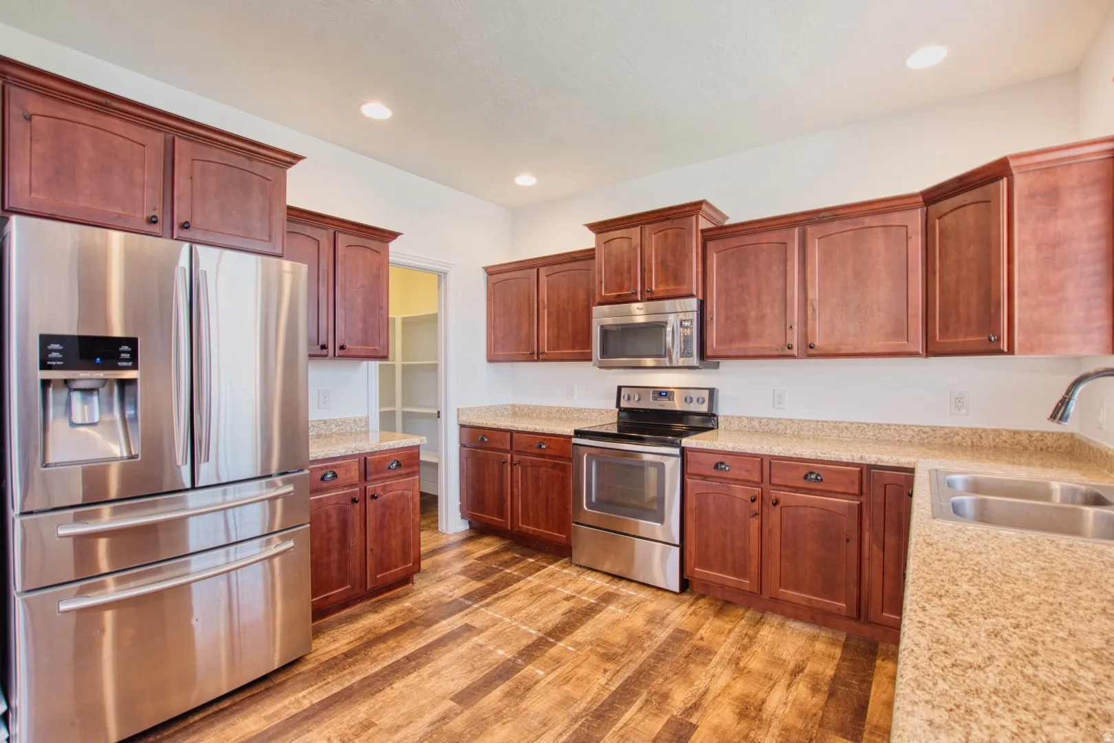 Kitchen featuring wood-finish flooring, cherry-stained cabinetry, stainless steel appliances, speckled countertops, and a walk-in pantry