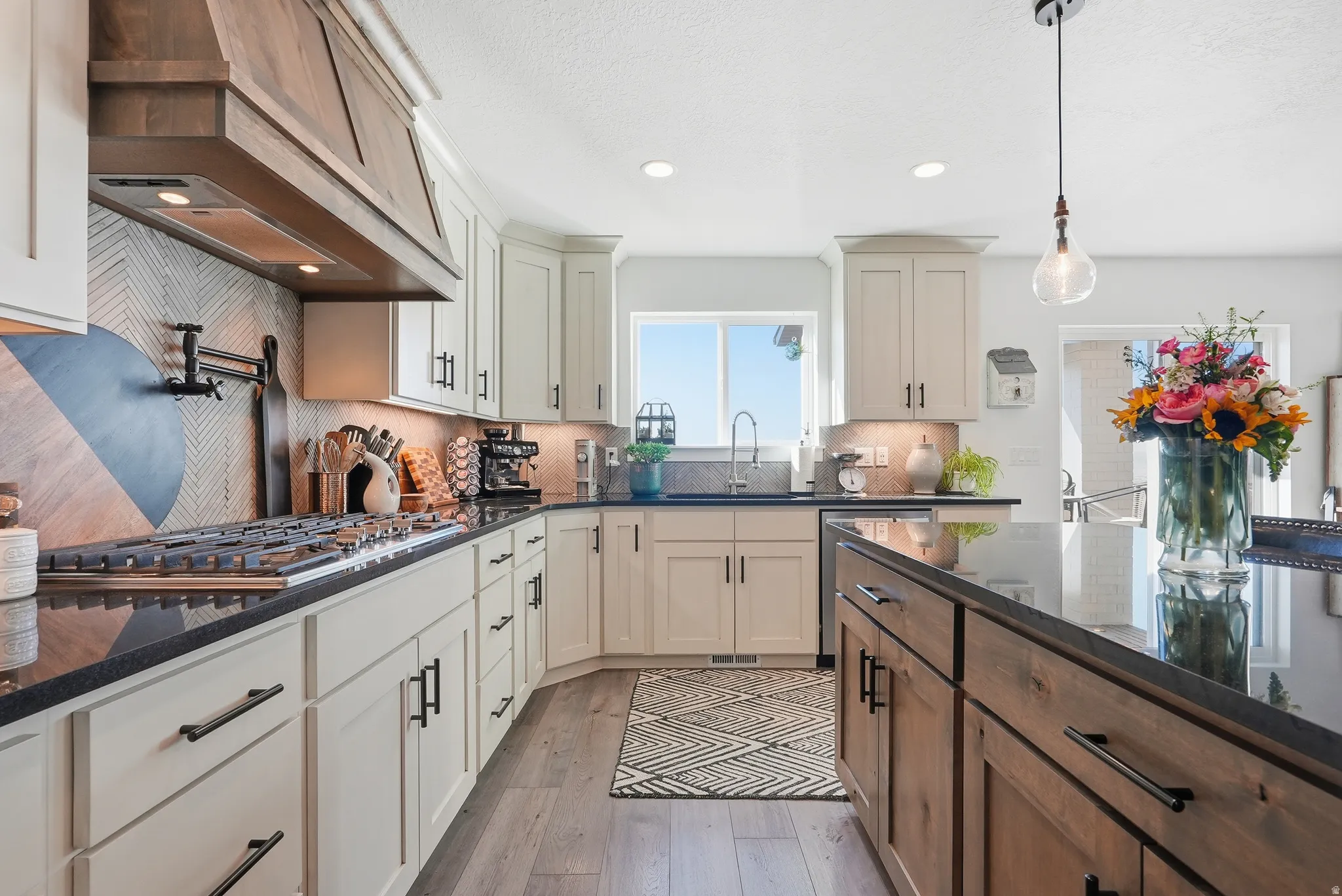 Spacious kitchen featuring light-toned cabinetry with matte black hardware, black countertops, and a wood-finish range hood