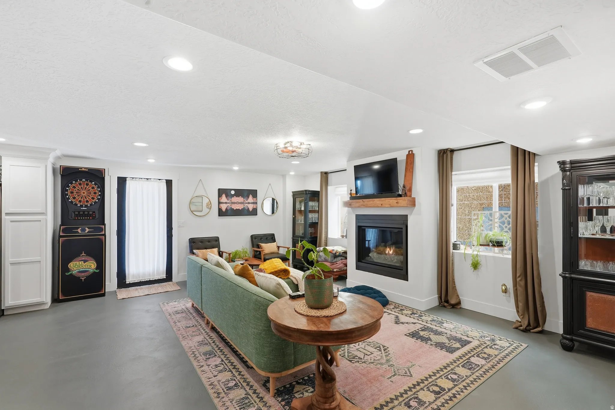 Recessed lighting illuminates this living space featuring a fireplace with a wood mantel, a built-in display cabinet, and a door to exterior