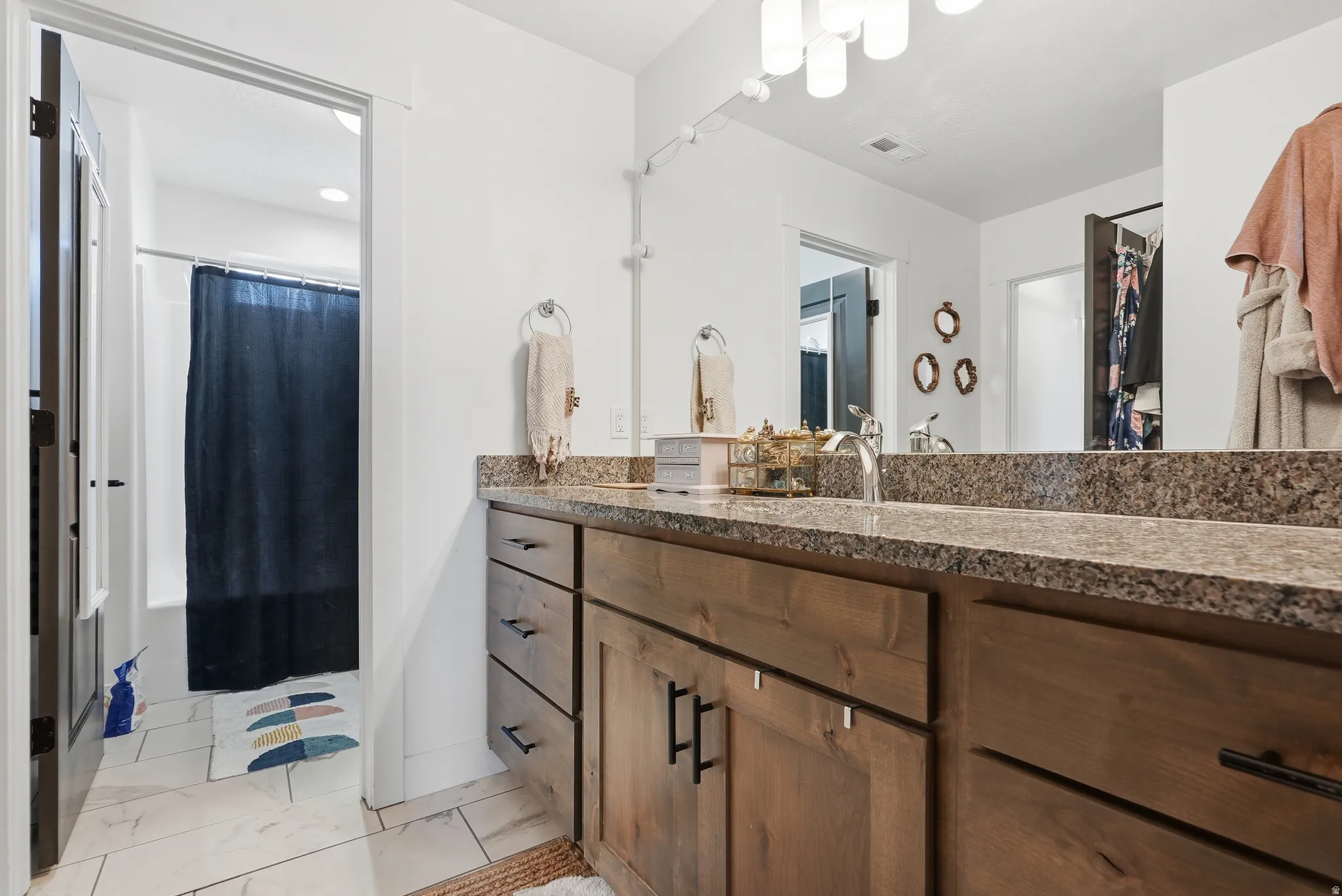 Bathroom featuring a wood-finish vanity with dual sinks, speckled countertop, and a large mirror