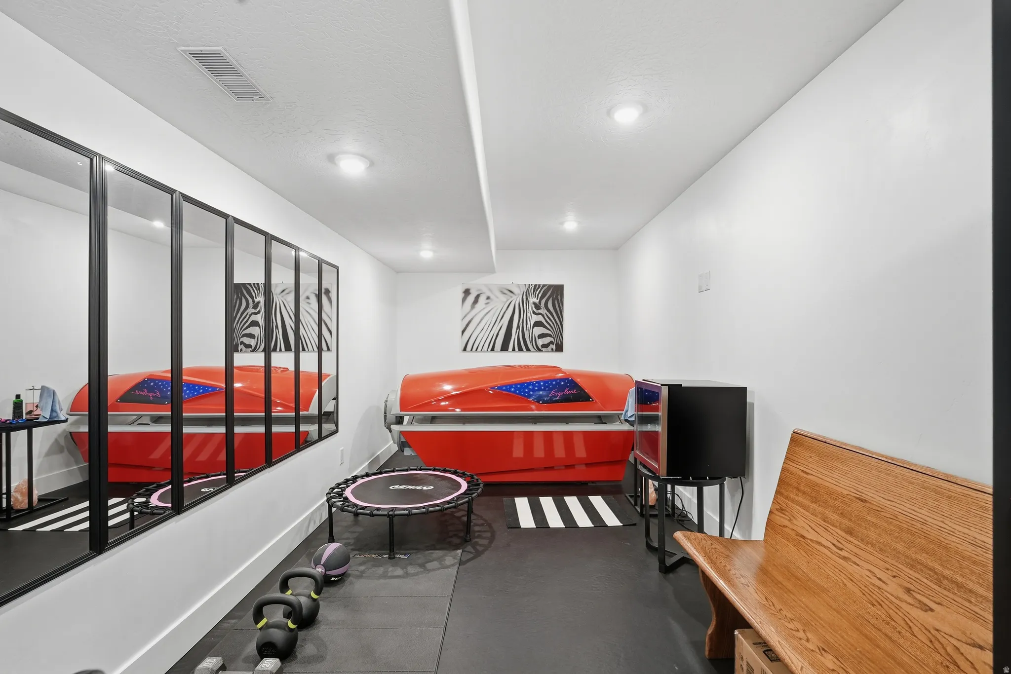 Dedicated fitness area featuring durable black rubber flooring, a full wall of framed mirrors, and recessed ceiling lighting