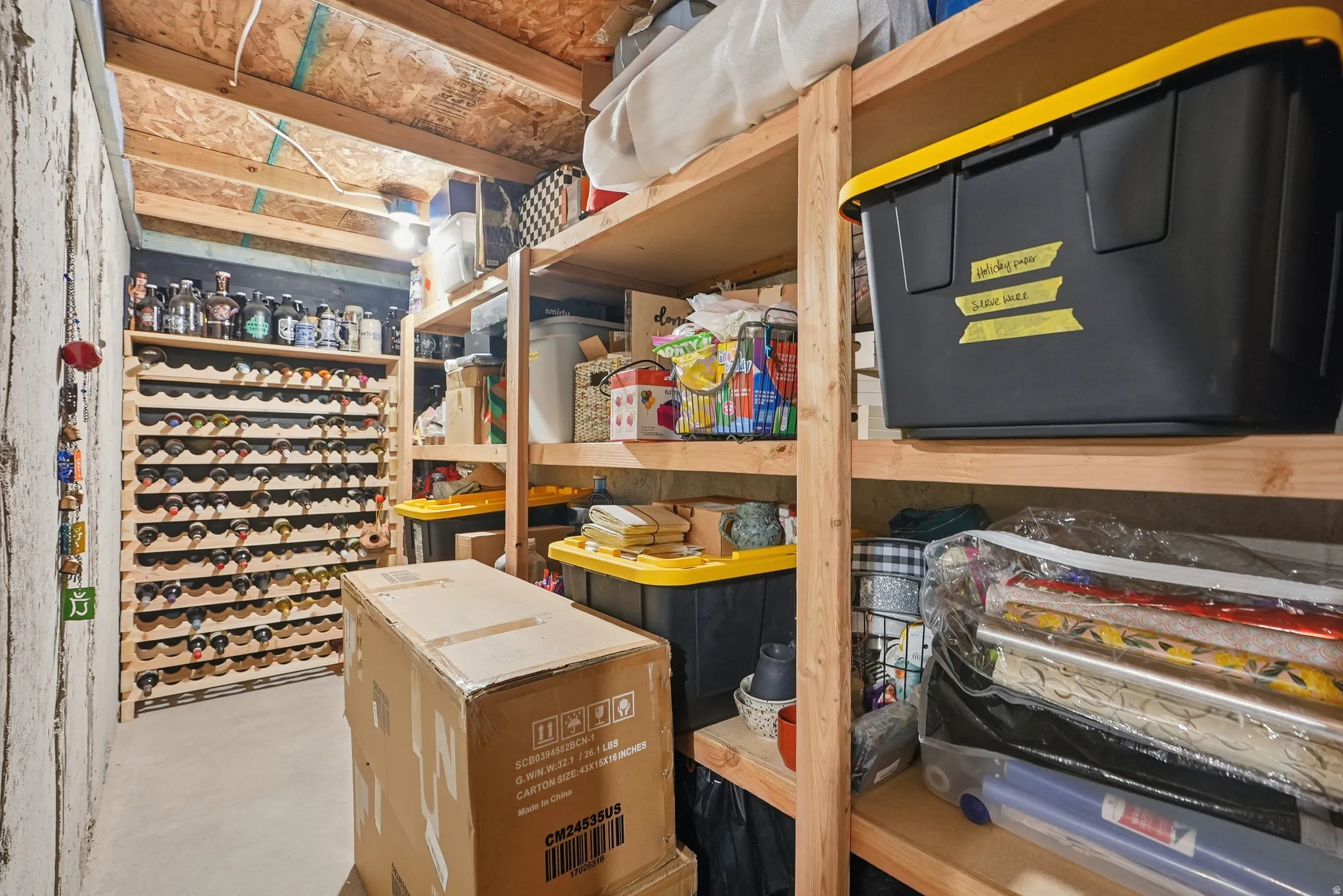 Dedicated storage area featuring an extensive built-in wine rack, exposed wood ceiling joists, and sturdy wood shelving