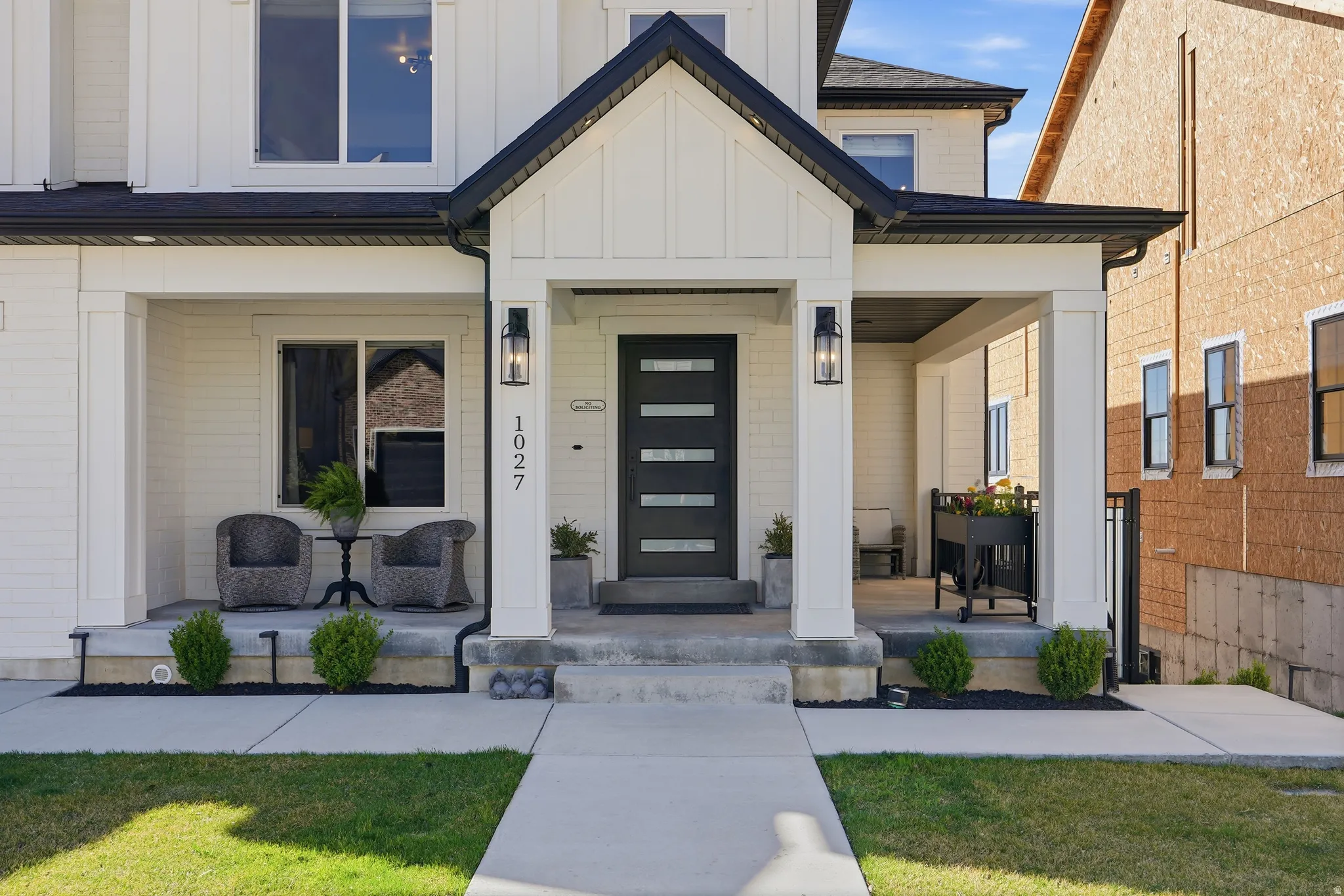 Modern farmhouse exterior featuring a covered porch, white board and batten siding, black trim, and a contemporary entry door with frosted glass inserts