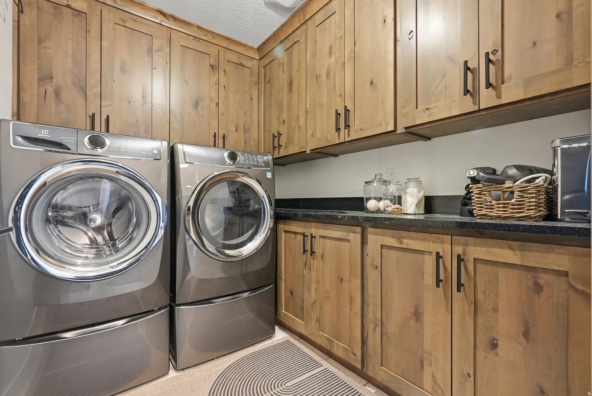 Laundry area featuring extensive wood cabinetry, dark countertops, and tile flooring