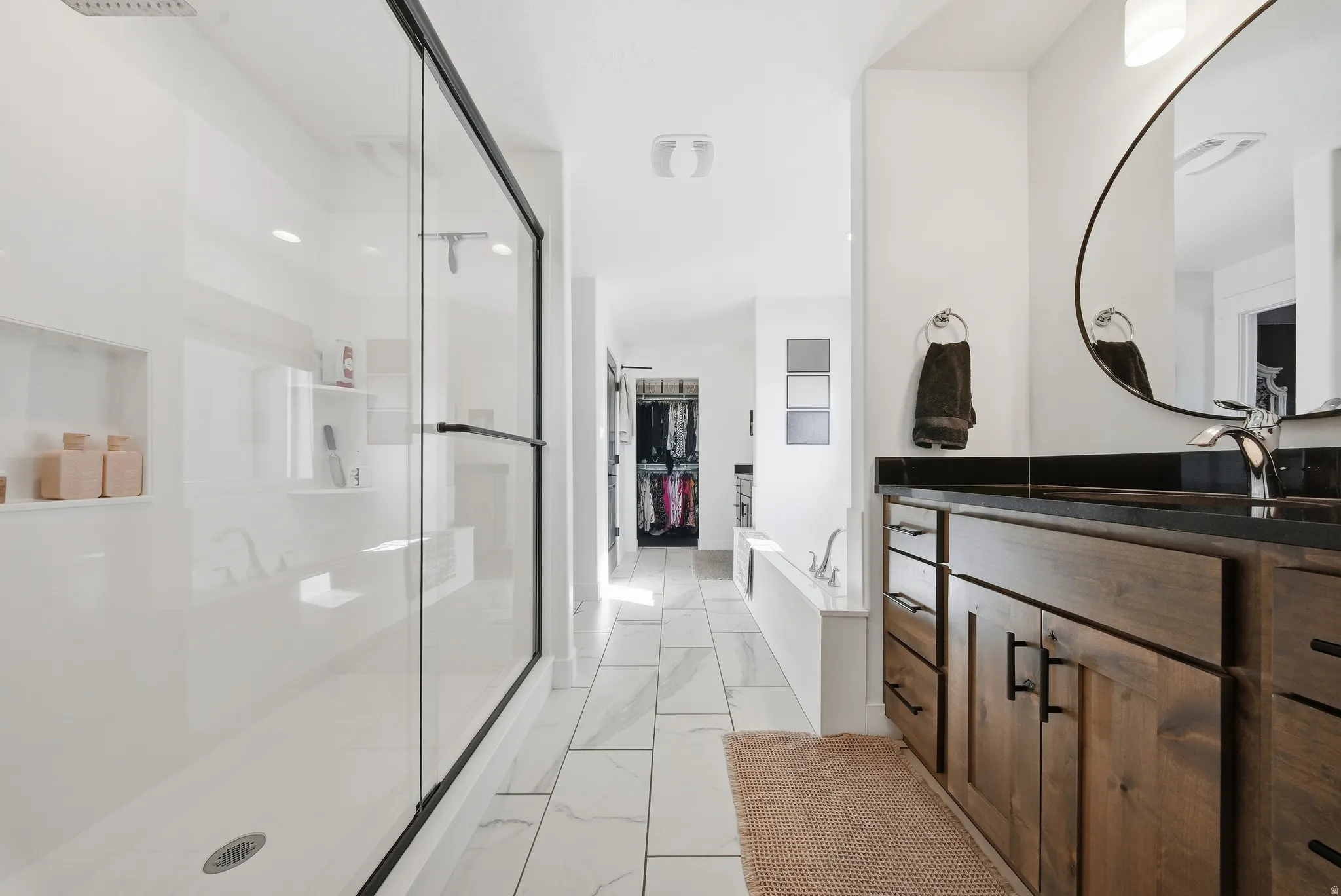 Modern bathroom featuring a spacious walk-in shower with clear glass enclosure and built-in shelving, a large soaking tub, and a wood-finish vanity with a dark countertop