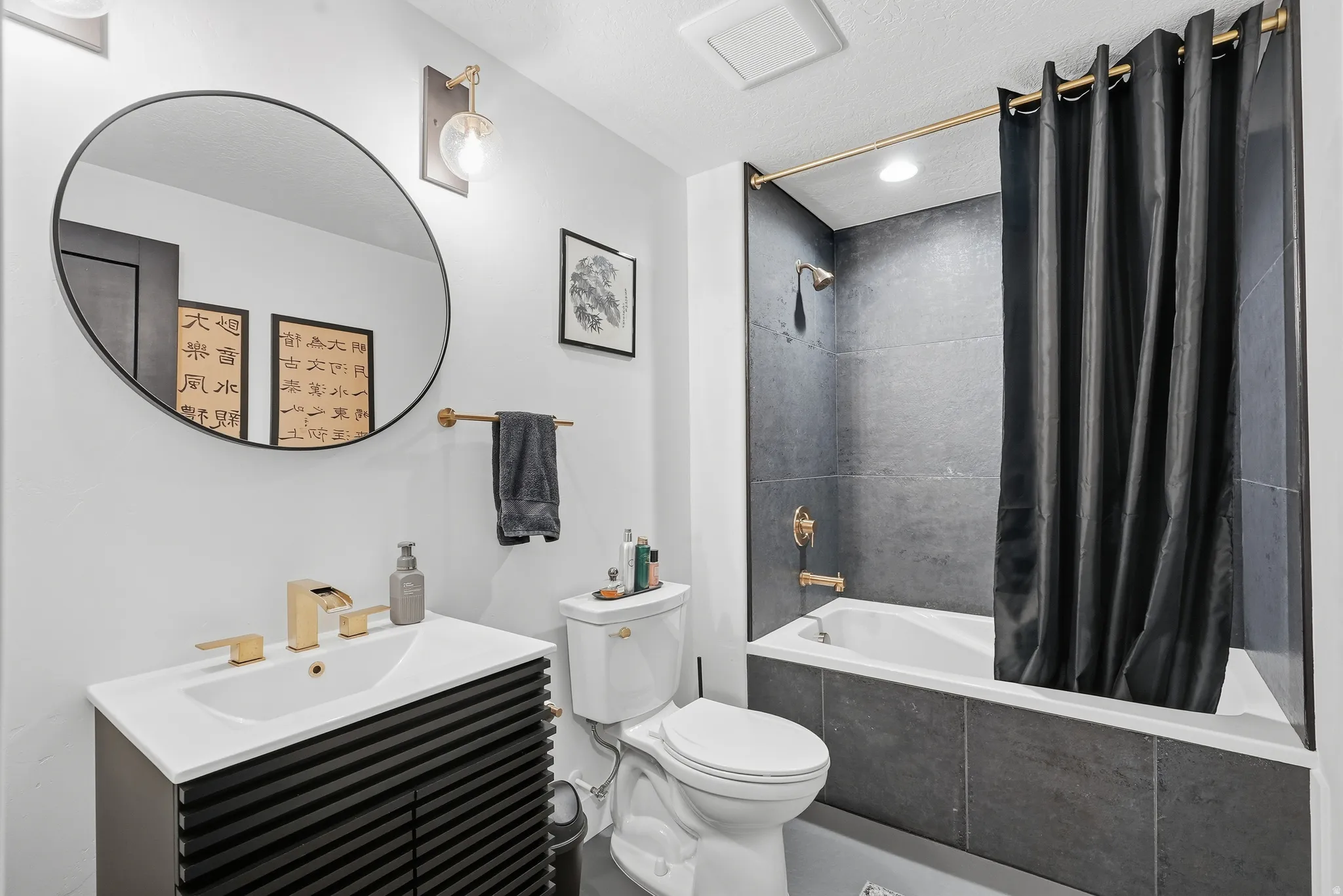 Bathroom featuring a black slatted vanity with a white integrated sink, gold-tone faucet, and a large round mirror