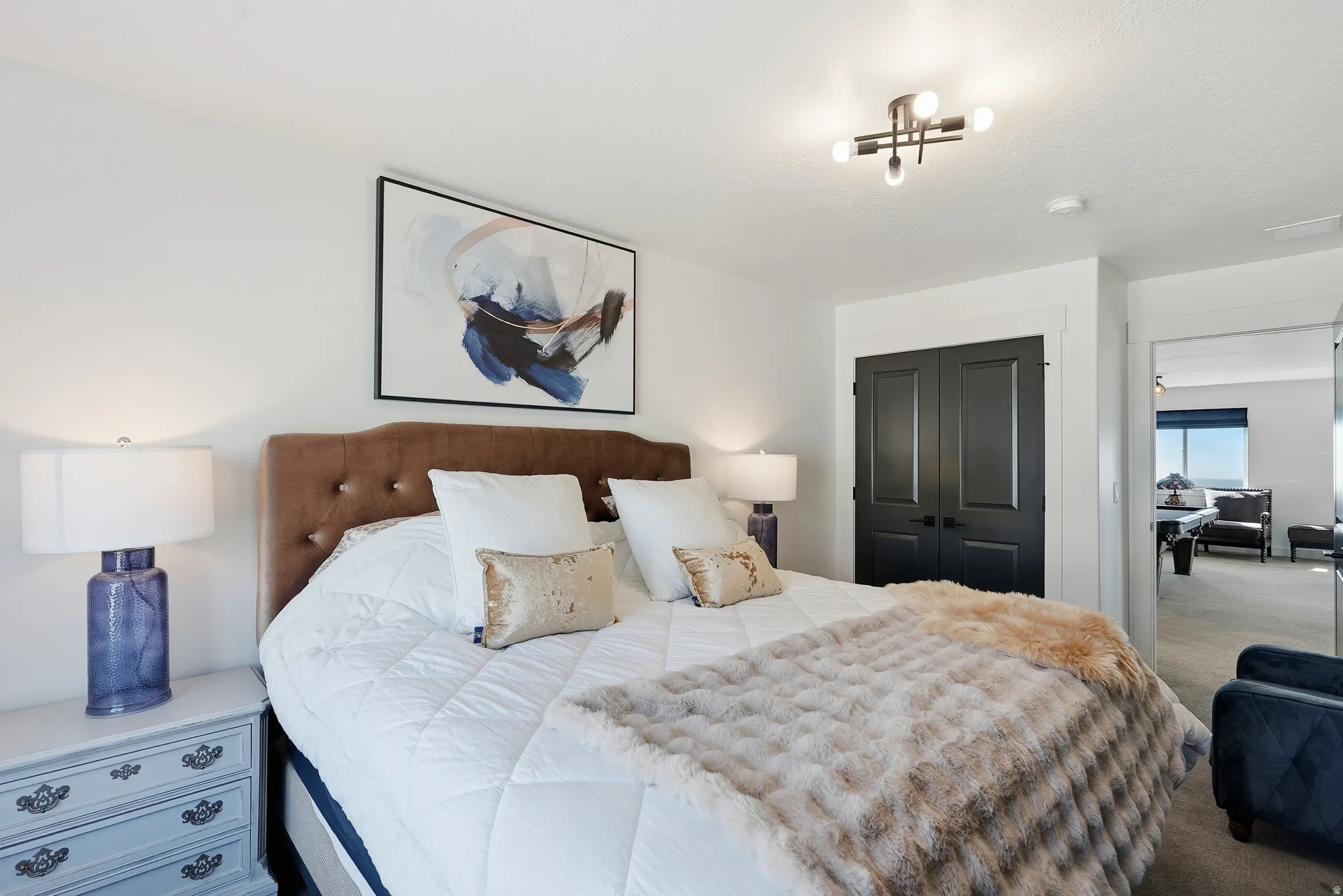 Spacious bedroom featuring an upholstered headboard, dual-panel doors, and an overhead light fixture