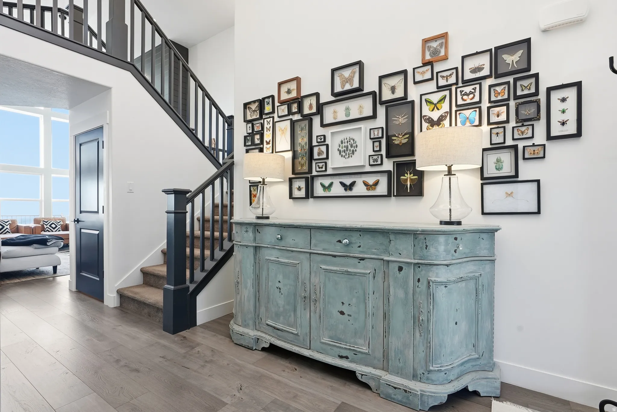 Spacious entry hall featuring light wood-finish flooring, a two-story staircase with dark banisters, and a solid black door