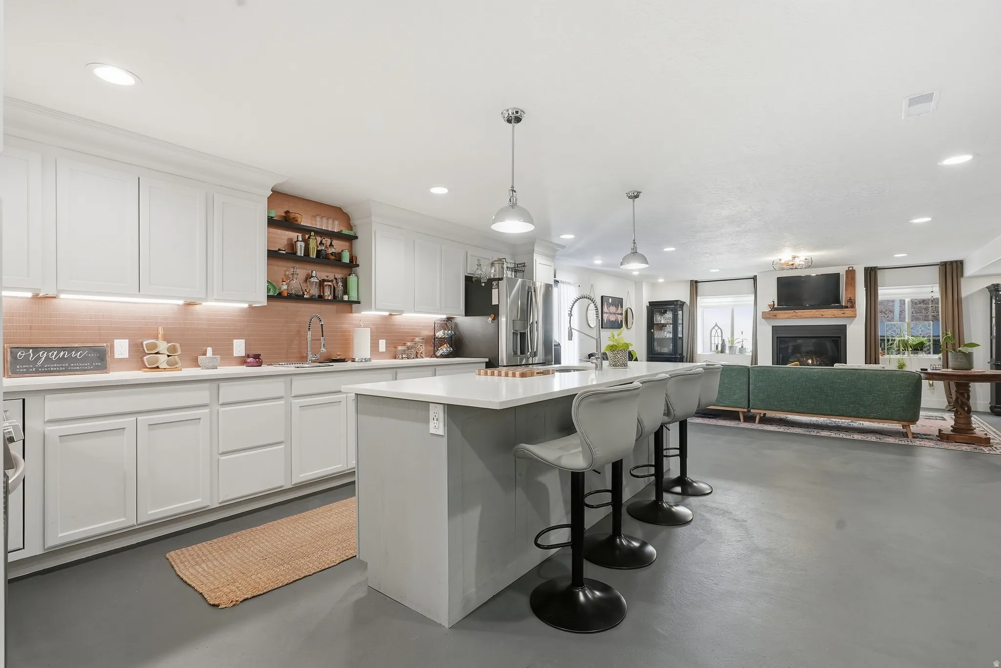 Open-concept living area featuring a kitchen island with seating, pendant lighting, white cabinetry, a tiled backsplash, and a fireplace with a wood mantel