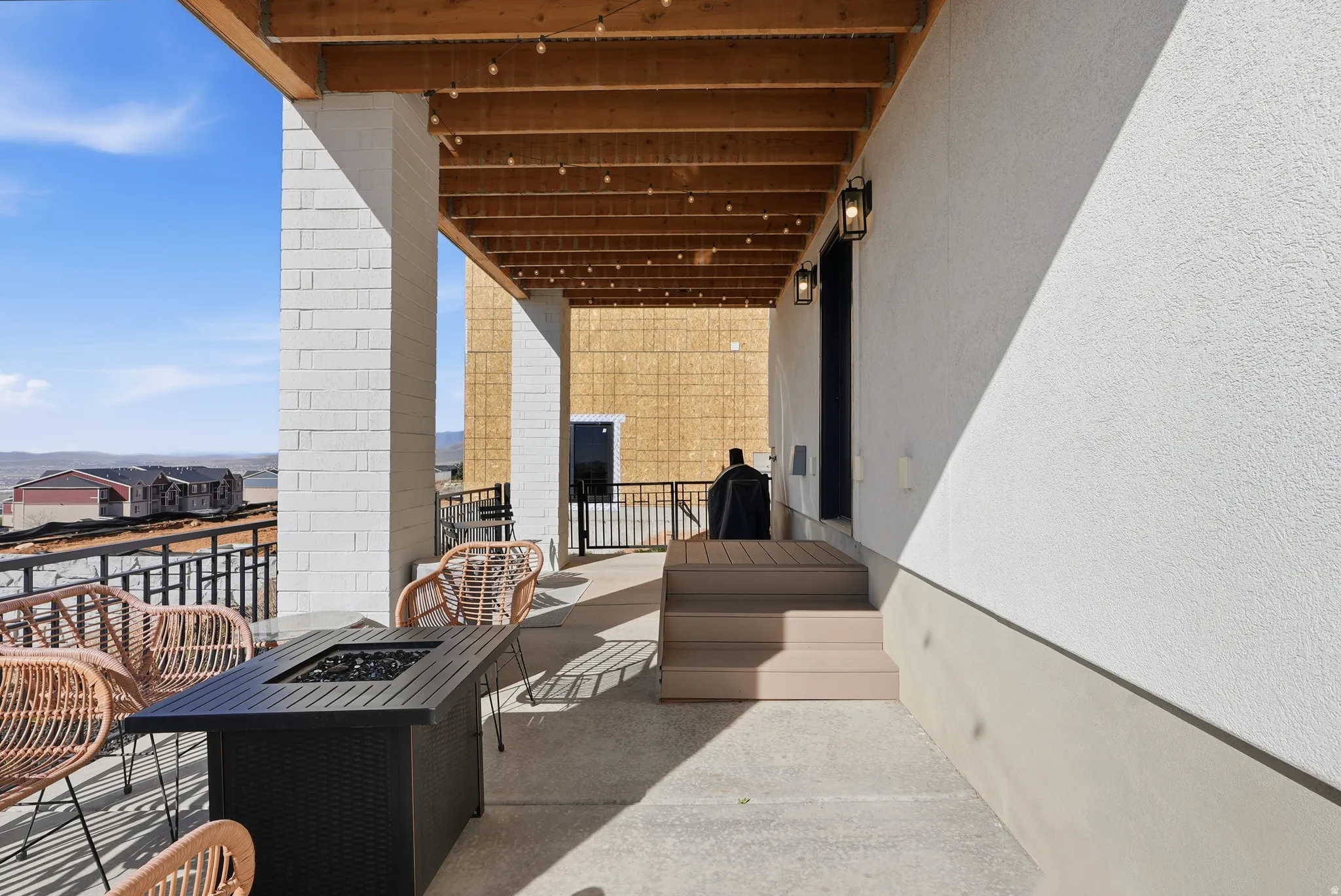 Expansive covered patio featuring a concrete surface, white textured exterior walls, and a wood-beamed ceiling with string lighting