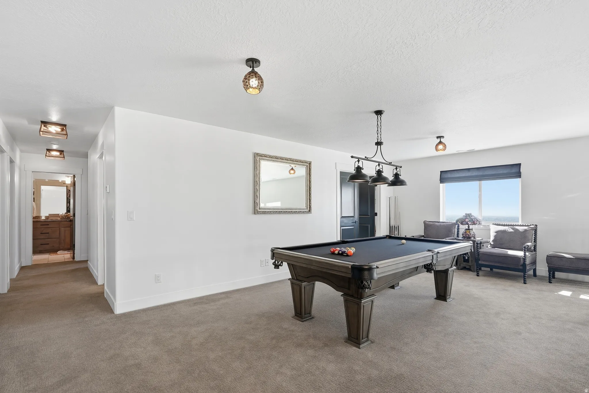 Spacious room with plush carpeting, featuring a pool table with an industrial-style overhead light fixture