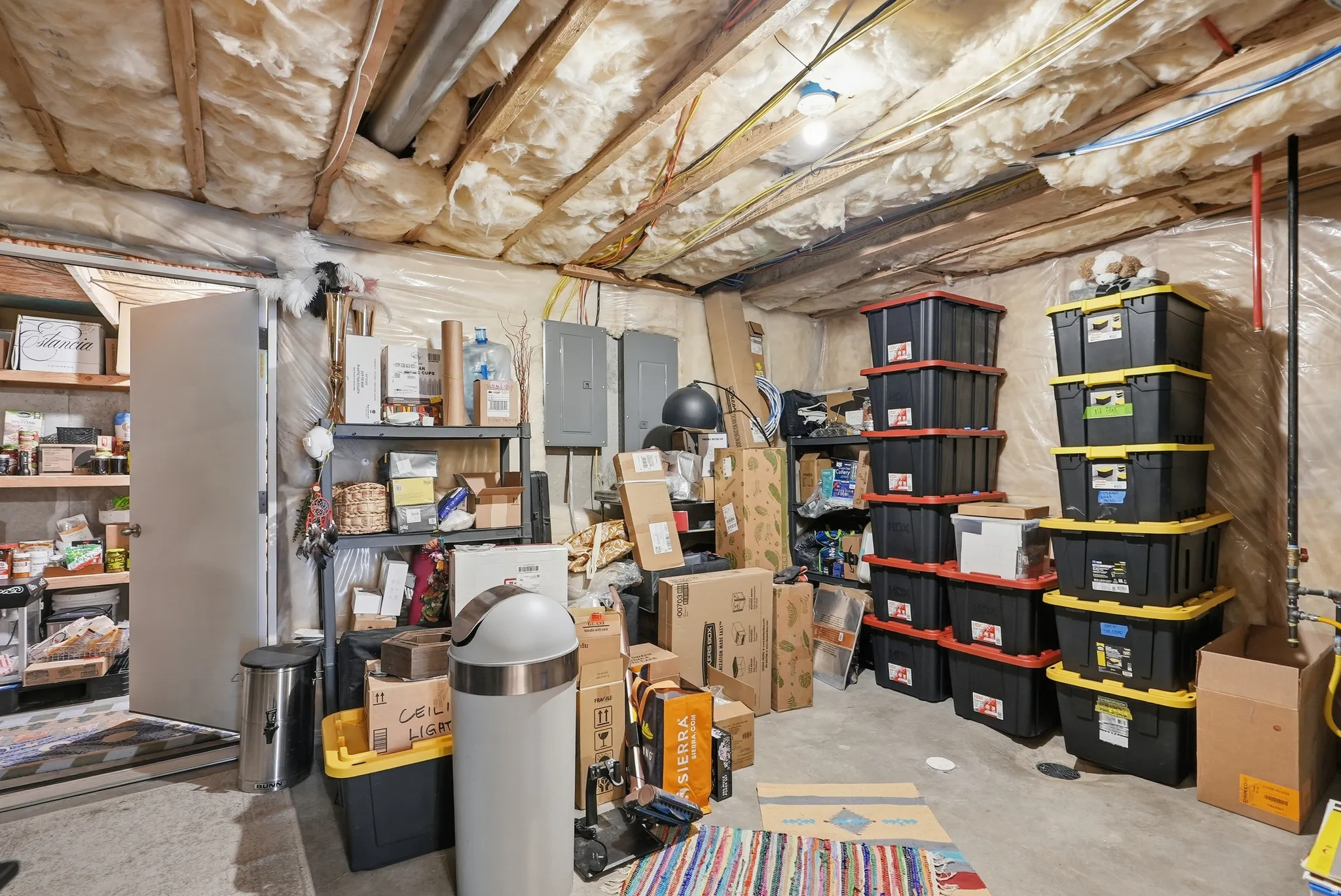 Unfinished basement area featuring exposed ceiling joists with insulation, concrete flooring, and visible utility lines