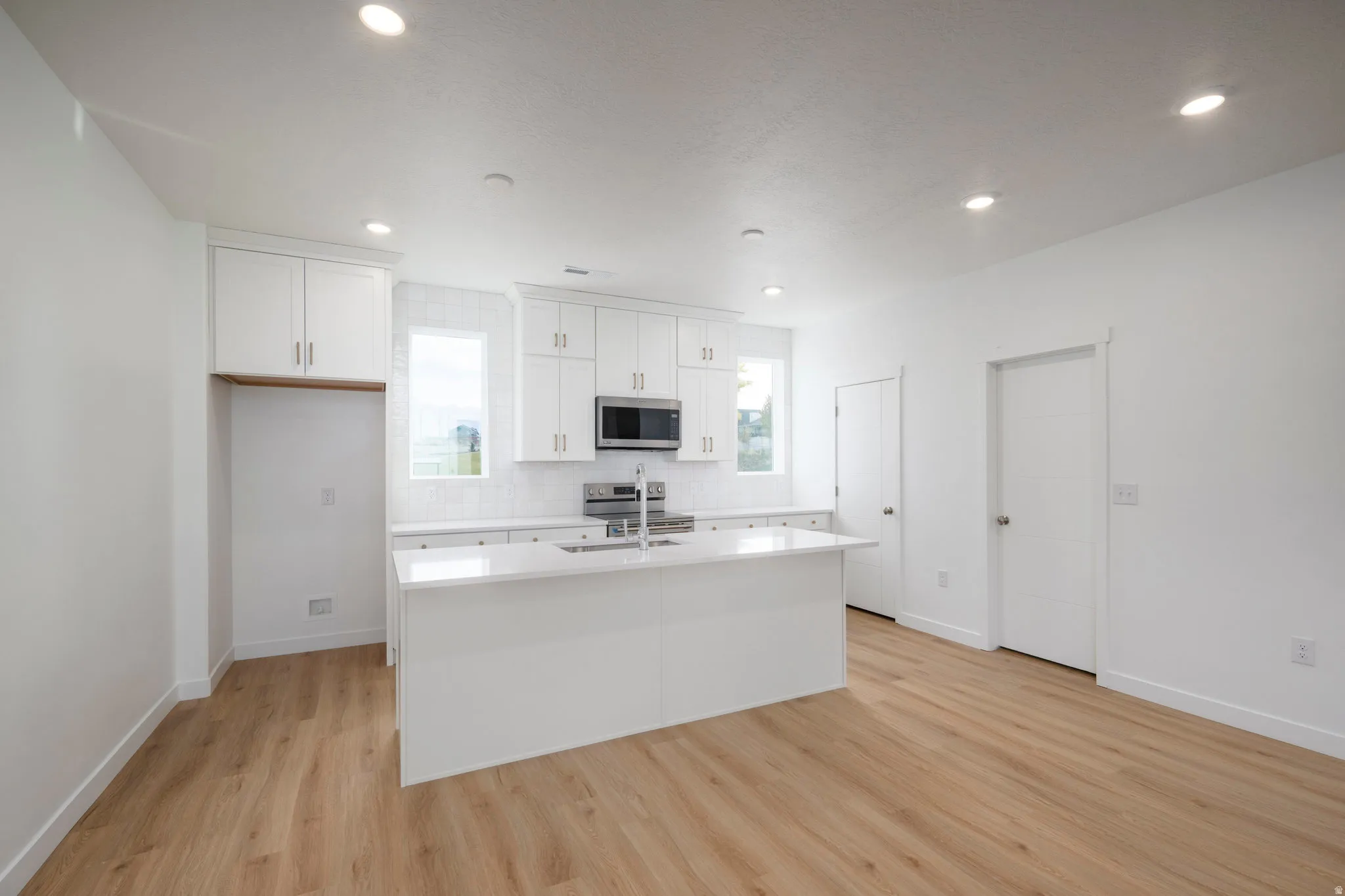 Open-concept kitchen featuring a central island with a solid surface countertop, white cabinetry with contemporary hardware, stainless steel appliances, and wood-finish flooring