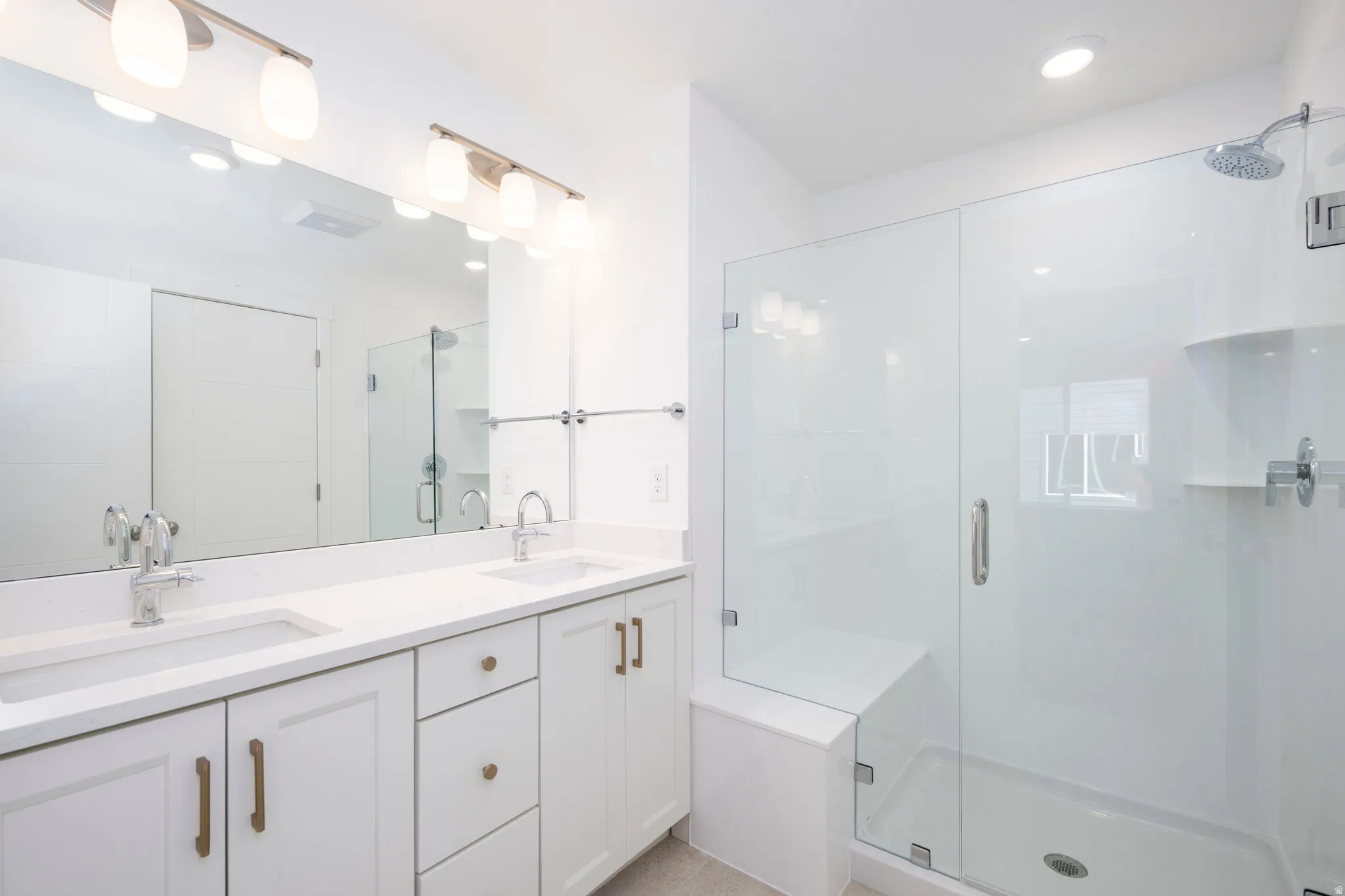 Contemporary bathroom featuring a spacious glass-enclosed shower with a built-in bench, dual vanity with undermount sinks, and white cabinetry with brass hardware
