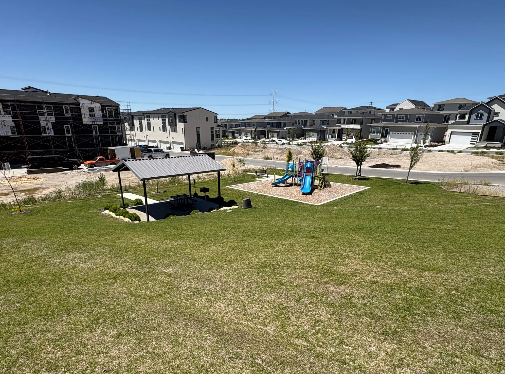Expansive green space featuring a covered picnic area with a built-in grill and a dedicated playground with slides and climbing elements