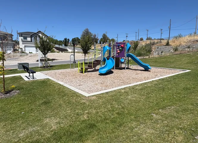 Community playground area featuring a colorful playset with slides, climbing elements, and a wood chip surface