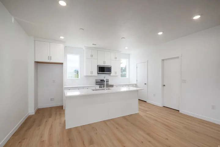 Open-concept kitchen featuring a central island with a solid surface countertop, white cabinetry with contemporary hardware, stainless steel appliances, and wood-finish flooring