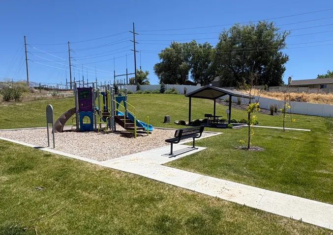 Community park area featuring a playground with a slide and climbing features, a covered picnic area with seating, and a paved pathway